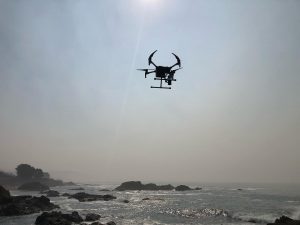 A drone hovers over a rocky coast.