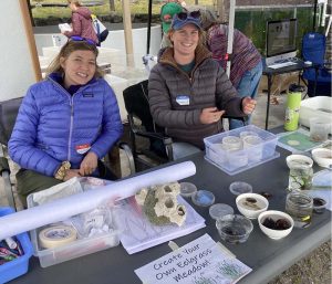 Becca Maher and Maddie Hollister sitting at a display table at Friday Harbor Labs' annual Open House.