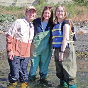 Undergrad and graduate teaching assistants pose on a Friday Harbor Labs beach with a course student, all wearing waterproof waders.