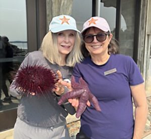 Two women holding a sea urchin and a sea star, wearing UW Friday Harbor Labs hats.