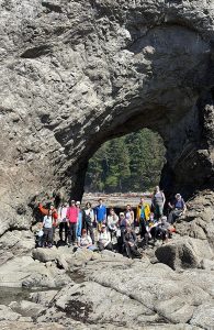 A group of people pose in front of a rock arch during a fieldtrip to the outer Washington coast.